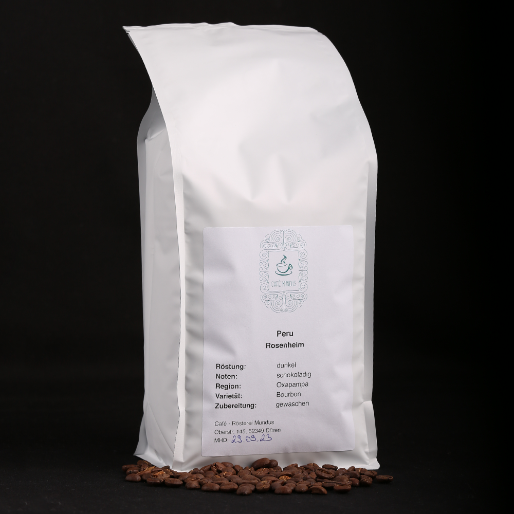 Eine weiße 1000g-Tüte mit Peru Rosenheim Kaffee aus der Rösterei Mundus mit einigen davor liegenden Kaffeebohnen